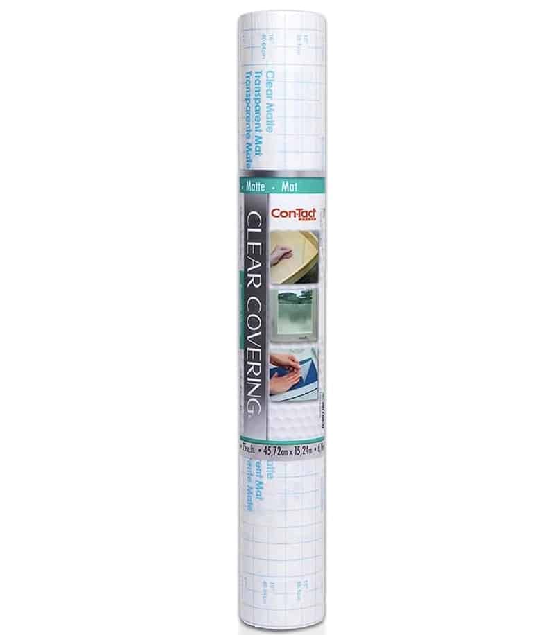 A roll of Con-Tact Brand clear covering adhesive paper with a matte finish, featuring a grid-lined backing for easy measuring and cutting—perfect for creating easy corkboard placemats. The packaging shows example uses for the product.